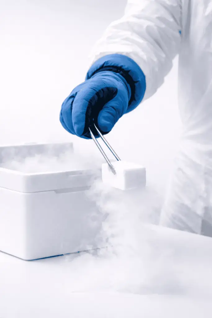 Person mit Schutzhandschuhen hält Trockeneis mit Zange – sicherer Umgang mit Trockeneis